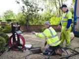 Two men in high visibility gear using CCTV drain equipment to inspect a drain 
