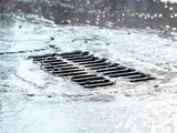 The grate of the storm sewer with water flowing 